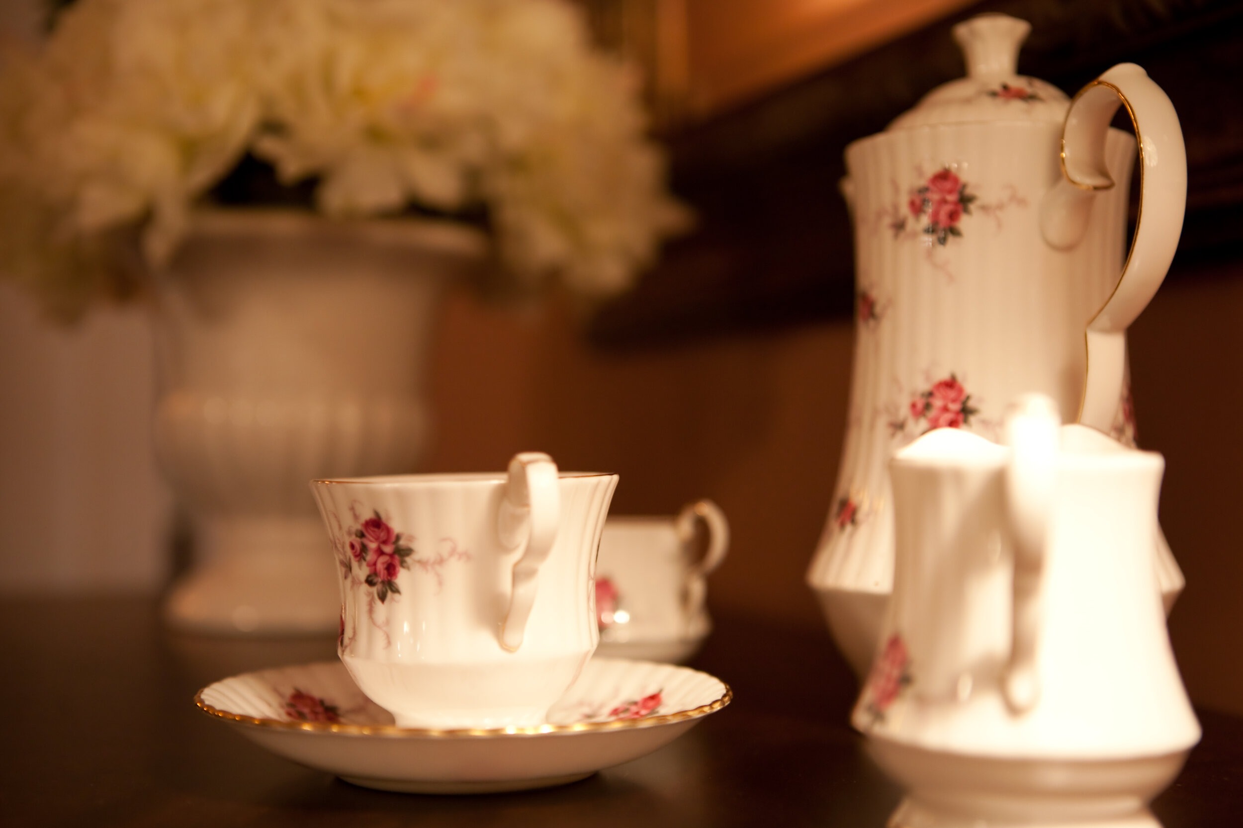 China tea pot, cups, and creamer with flowers in background